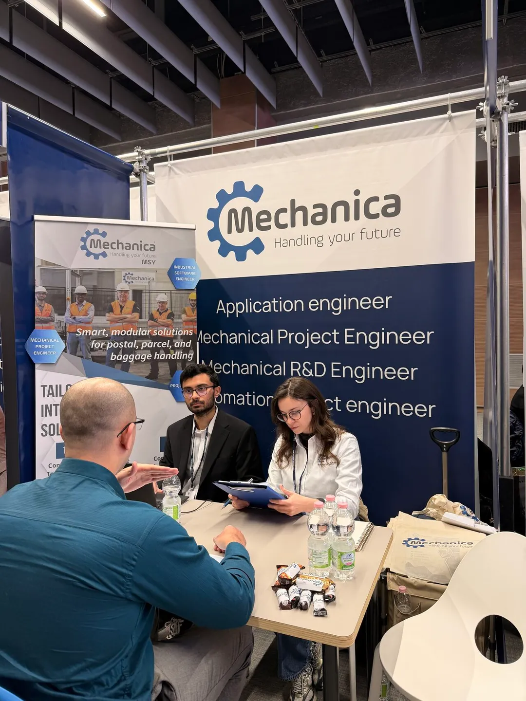 Interview in progress in front of the Mechanica roll-up