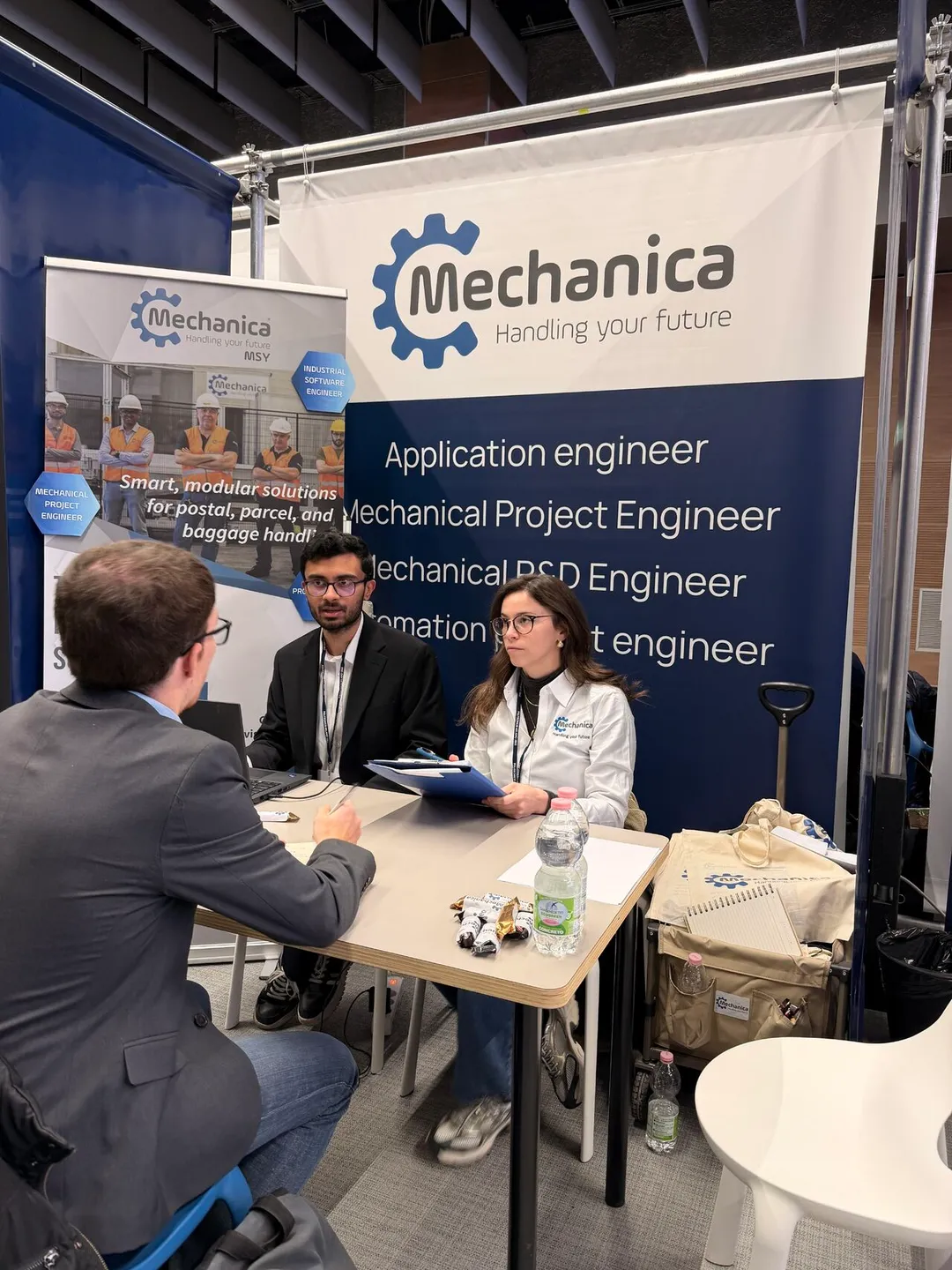 The Mechanica booth with the four open roles on the banner